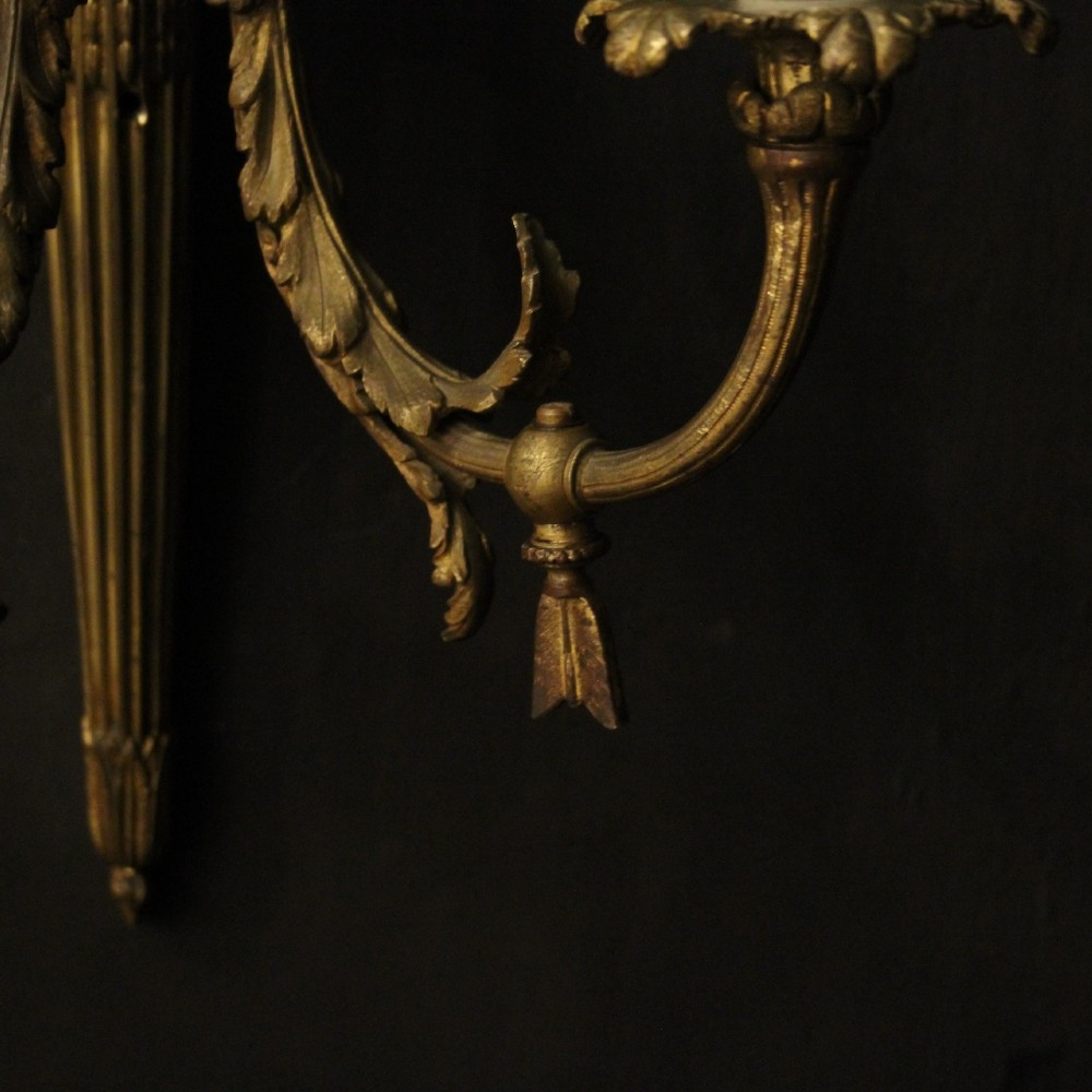 A pair of French gilt bronze two-light wall sconces featuring ribbon bow crestings and fluted tapering backplates mounted on a dark background. View IX