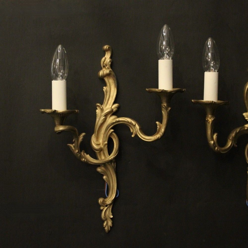 A pair of French gilt bronze twin-arm wall lights with scrolling acanthus leaf ornamentation and white candle sleeves. View II