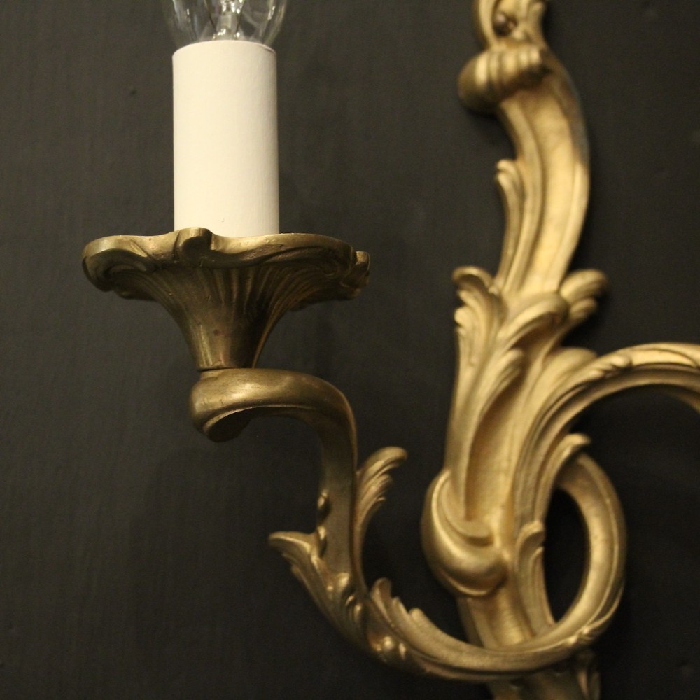 A pair of French gilt bronze twin-arm wall lights with scrolling acanthus leaf ornamentation and white candle sleeves. View V