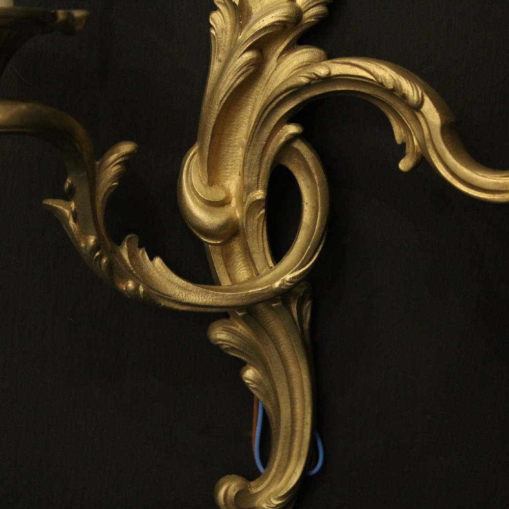A pair of French gilt bronze twin-arm wall lights with scrolling acanthus leaf ornamentation and white candle sleeves. View VII