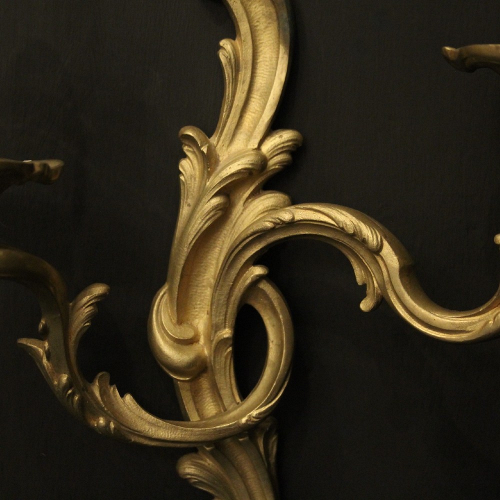 A pair of French gilt bronze twin-arm wall lights with scrolling acanthus leaf ornamentation and white candle sleeves. View VIII