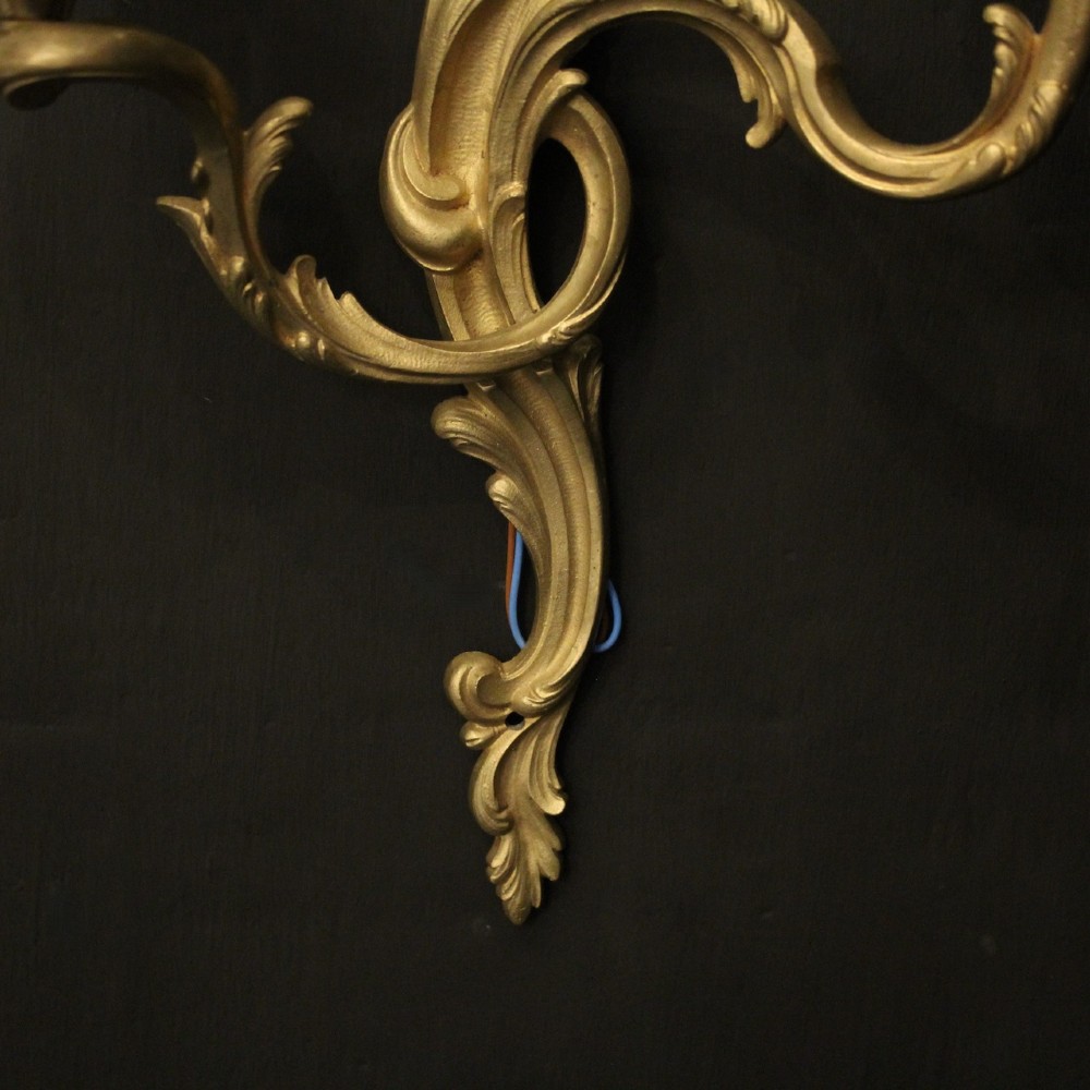 A pair of French gilt bronze twin-arm wall lights with scrolling acanthus leaf ornamentation and white candle sleeves. View IX