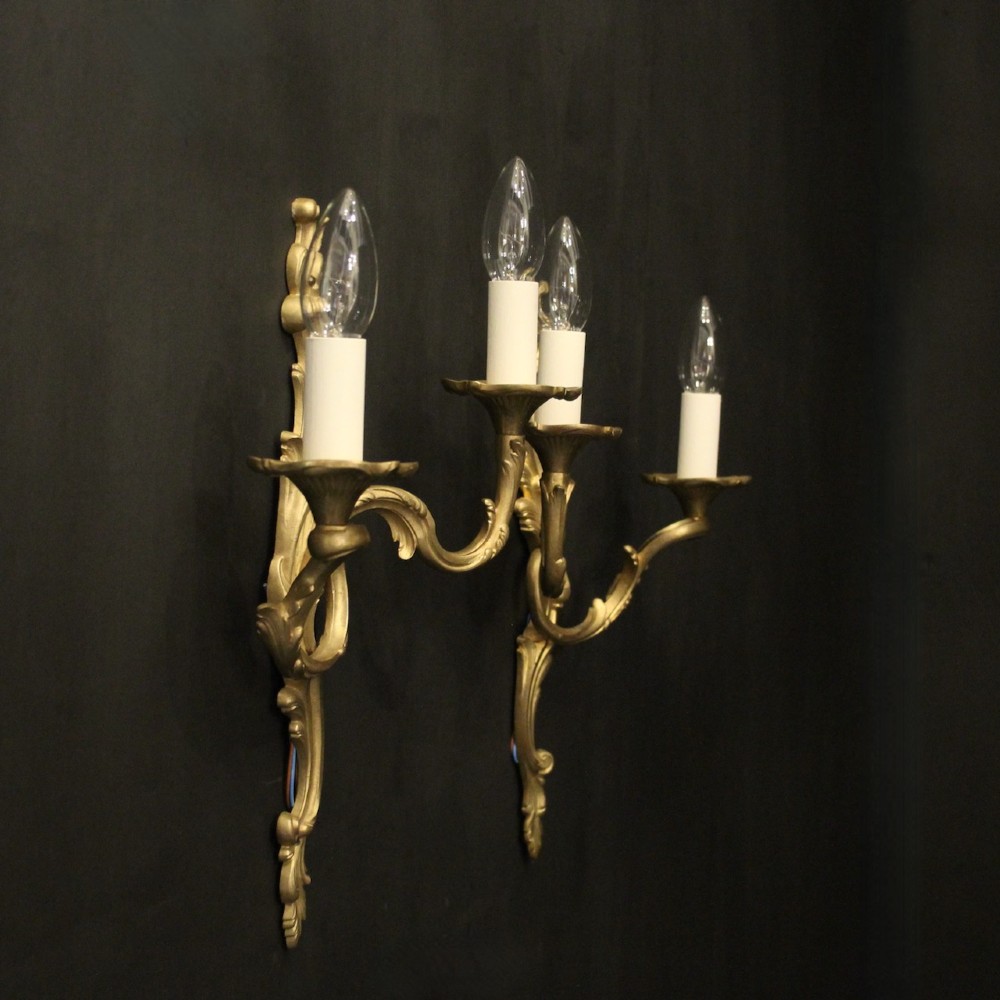 A pair of French gilt bronze twin-arm wall lights with scrolling acanthus leaf ornamentation and white candle sleeves. View X