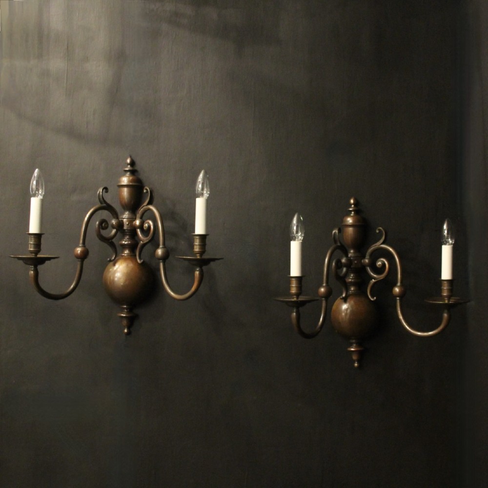 A pair of dark bronze twin-arm wall sconces featuring turned central shafts, scrollwork accents, and candle-style fittings.