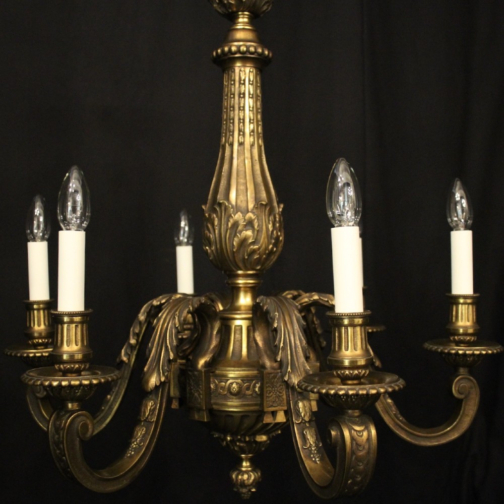 A nineteenth-century French gilded bronze chandelier with six curved arms featuring acanthus leaf motifs and white candle sleeves against a dark background. View II