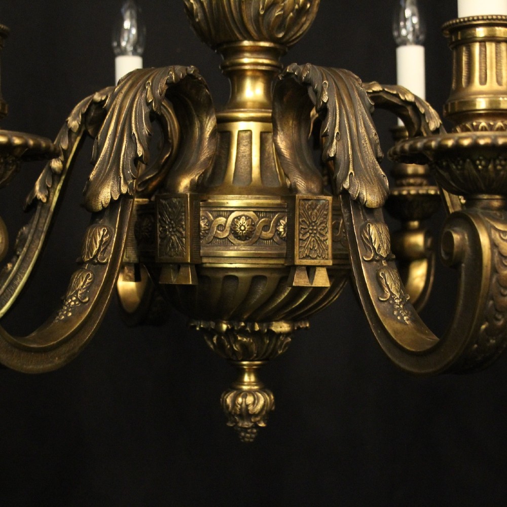A nineteenth-century French gilded bronze chandelier with six curved arms featuring acanthus leaf motifs and white candle sleeves against a dark background. View V