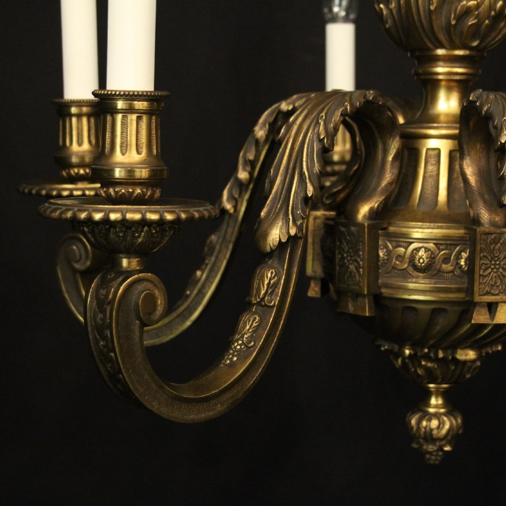 A nineteenth-century French gilded bronze chandelier with six curved arms featuring acanthus leaf motifs and white candle sleeves against a dark background. View VI
