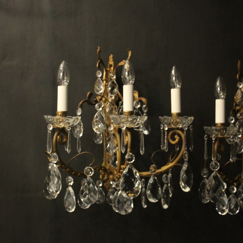 A pair of French gilded metal triple-arm wall sconces adorned with faceted crystal teardrop pendeloques and candle-style sockets. View II