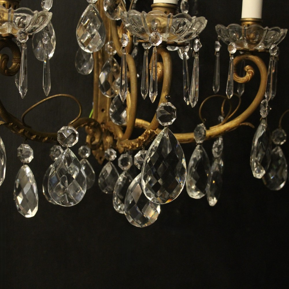 A pair of French gilded metal triple-arm wall sconces adorned with faceted crystal teardrop pendeloques and candle-style sockets. View V