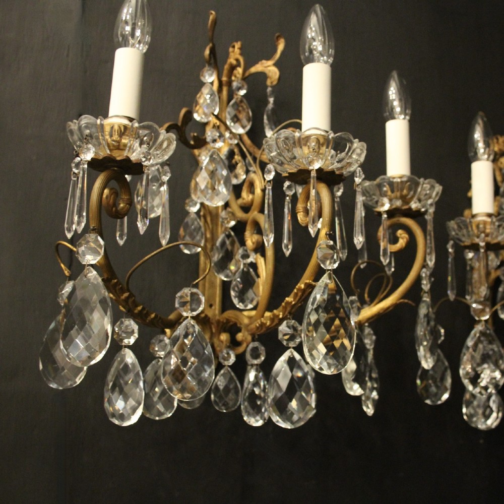 A pair of French gilded metal triple-arm wall sconces adorned with faceted crystal teardrop pendeloques and candle-style sockets. View VII