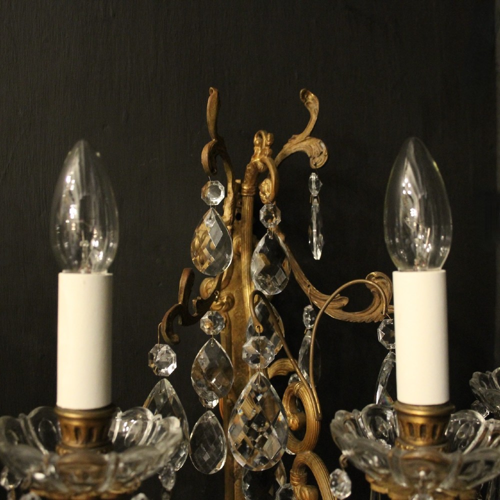 A pair of French gilded metal triple-arm wall sconces adorned with faceted crystal teardrop pendeloques and candle-style sockets. View IX