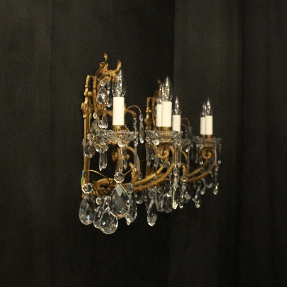 A pair of French gilded metal triple-arm wall sconces adorned with faceted crystal teardrop pendeloques and candle-style sockets. View X