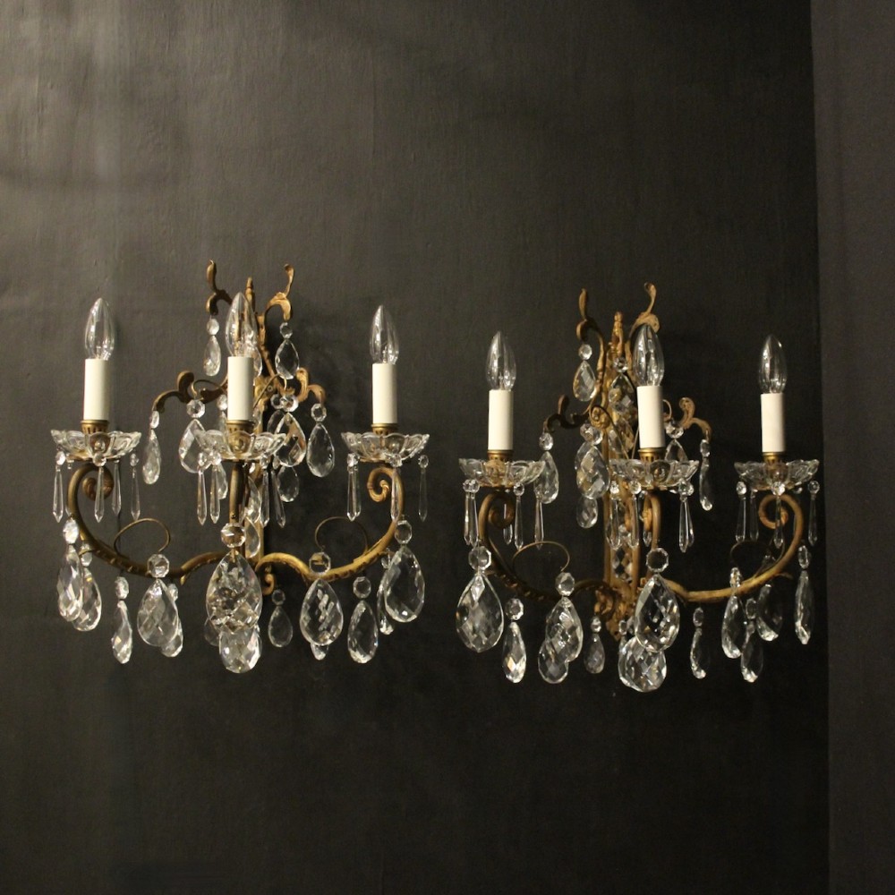 A pair of French gilded metal triple-arm wall sconces adorned with faceted crystal teardrop pendeloques and candle-style sockets.