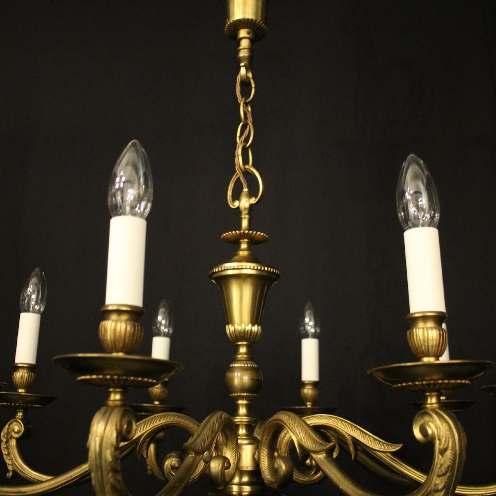 An eight-light antique gilded brass chandelier featuring ornate scrolled arms, candle-style sleeves, and a central turned baluster column. View II