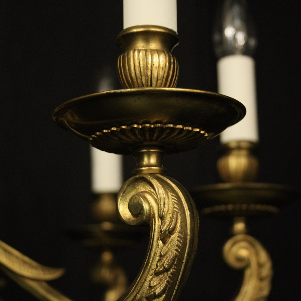 An eight-light antique gilded brass chandelier featuring ornate scrolled arms, candle-style sleeves, and a central turned baluster column. View V