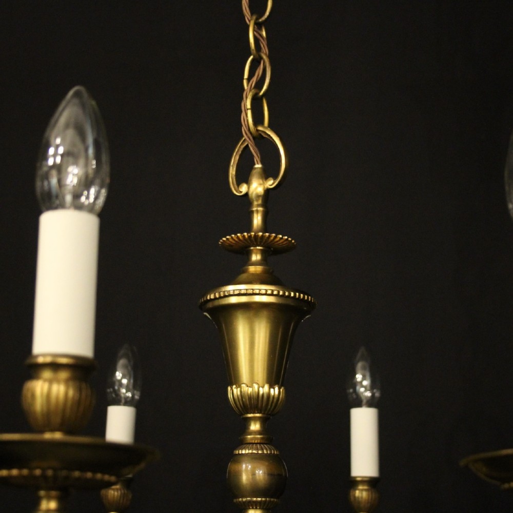 An eight-light antique gilded brass chandelier featuring ornate scrolled arms, candle-style sleeves, and a central turned baluster column. View VI
