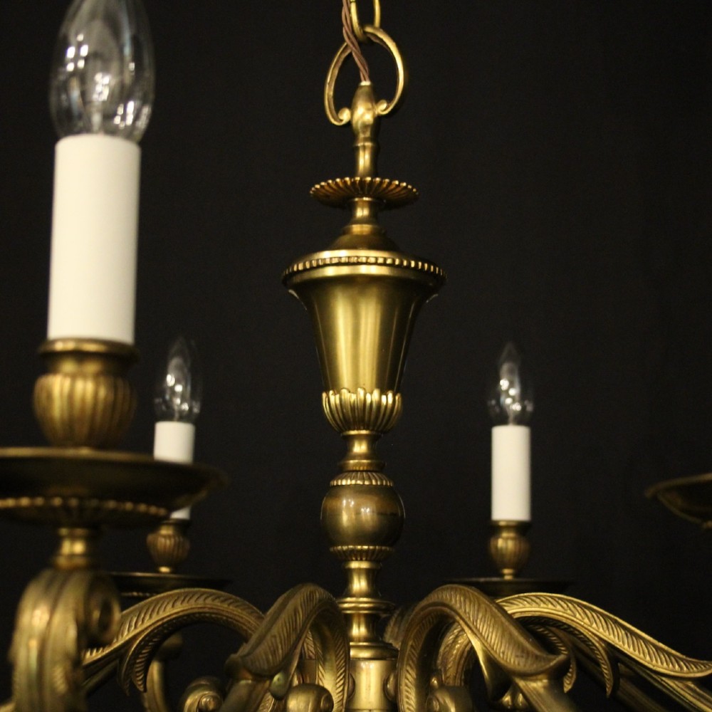 An eight-light antique gilded brass chandelier featuring ornate scrolled arms, candle-style sleeves, and a central turned baluster column. View VII