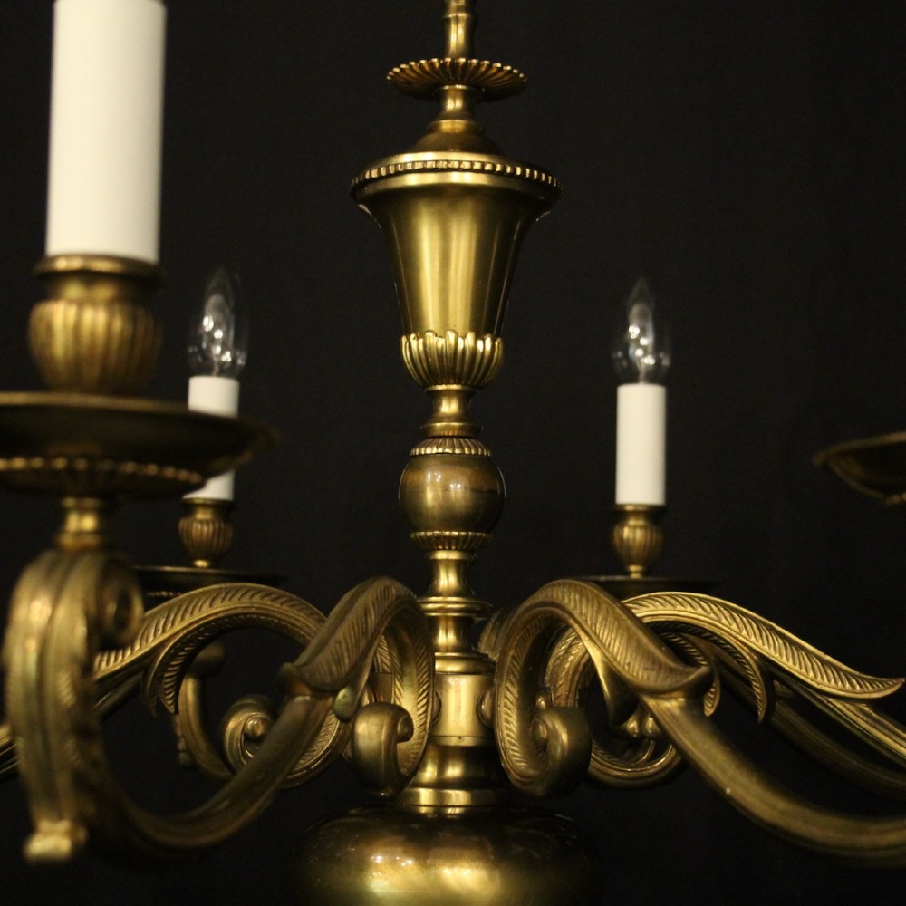 An eight-light antique gilded brass chandelier featuring ornate scrolled arms, candle-style sleeves, and a central turned baluster column. View VIII
