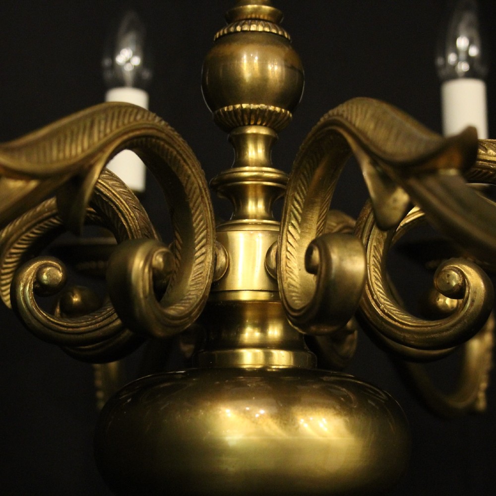 An eight-light antique gilded brass chandelier featuring ornate scrolled arms, candle-style sleeves, and a central turned baluster column. View IX