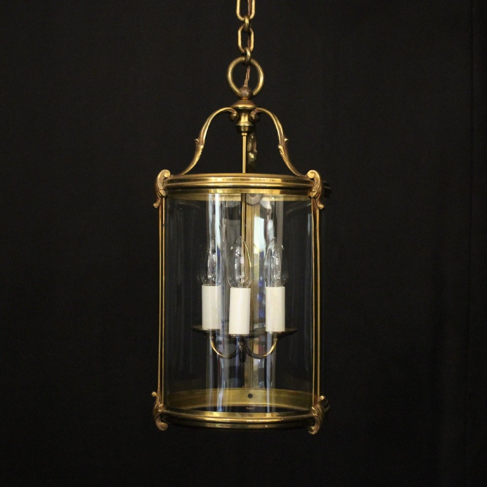 A cylindrical French hall lantern with a gilt brass frame, convex glass panels, and an internal three-light candelabra fitting suspended by a ring.