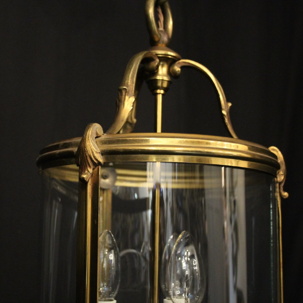 A cylindrical French hall lantern with a gilt brass frame, convex glass panels, and an internal three-light candelabra fitting suspended by a ring. View VI