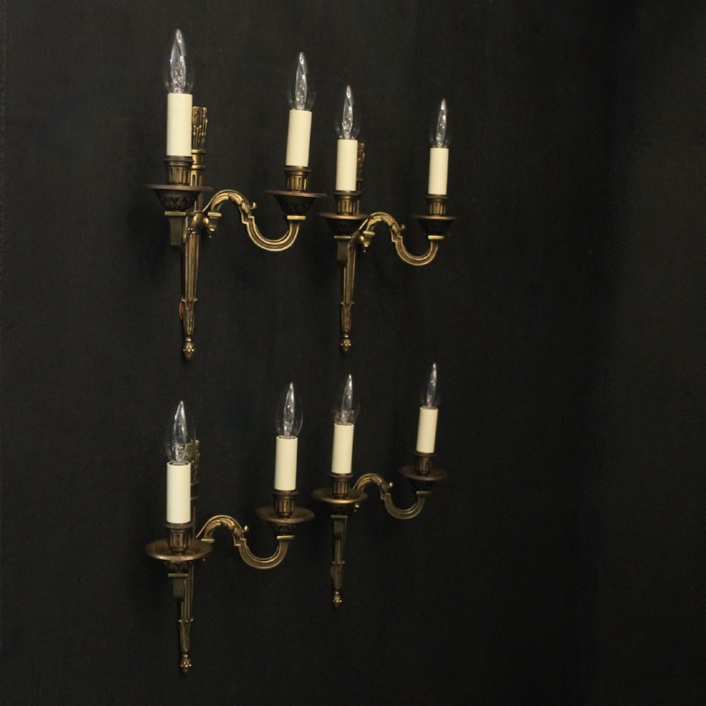 A set of four French Empire style gilded metal wall sconces, each featuring a central torch-shaped backplate and two curving candle arms. View X