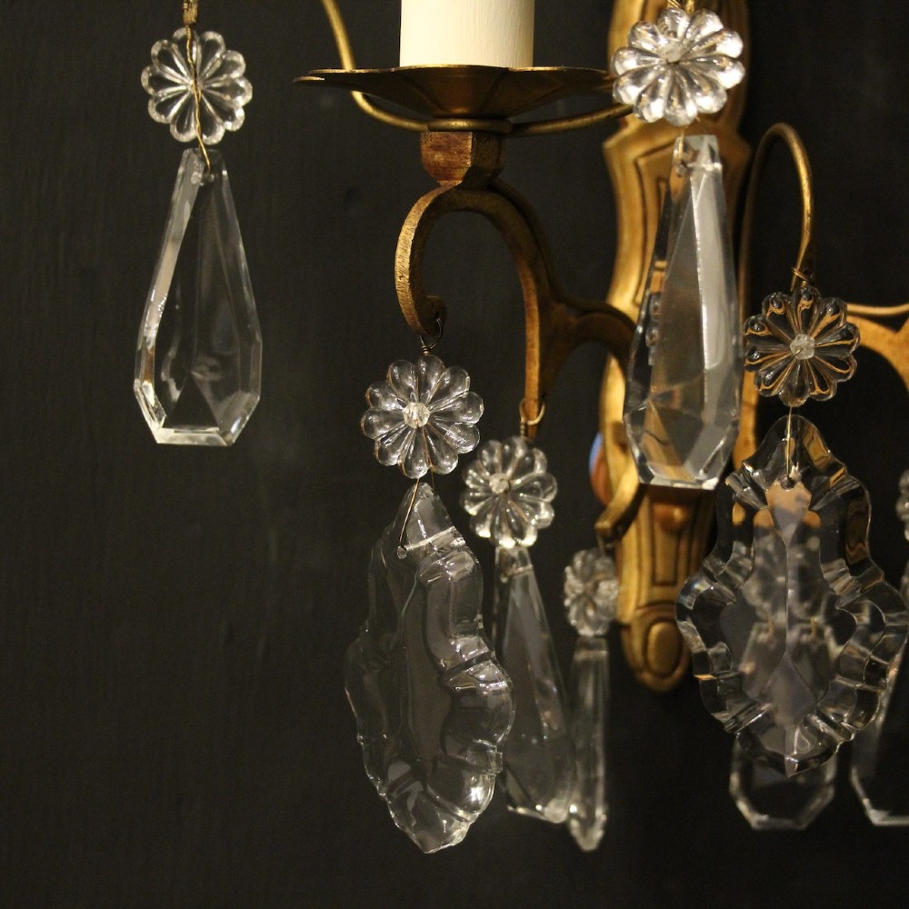 A pair of French gilded wall lights featuring twin candle-style bulb sockets, scrolling metal arms, and hanging faceted crystal droplets. View VII