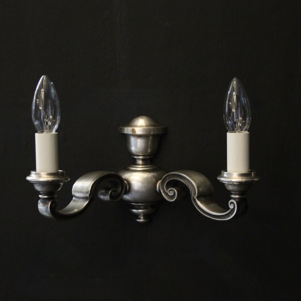 A pair of antique silver-plated twin-arm wall lights with scrolled branches, turned central urn backplates, and faux candle sleeves. View II