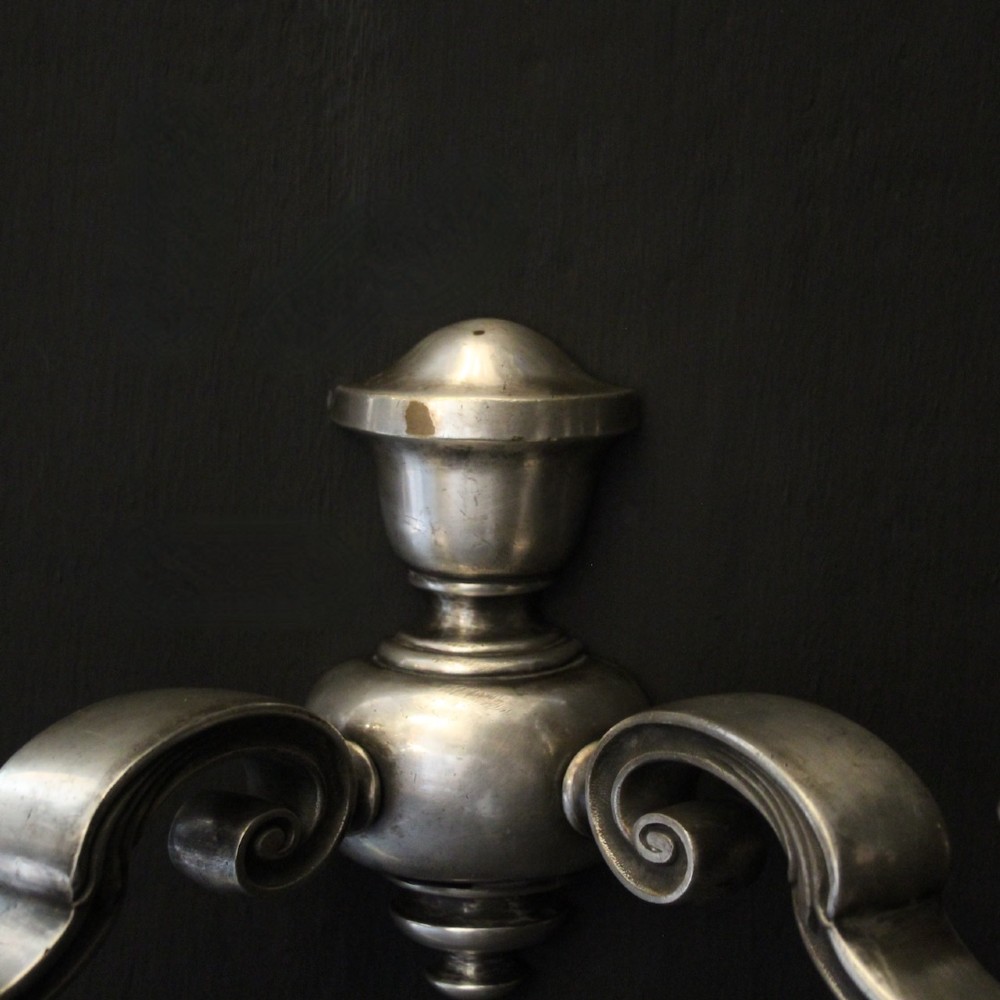A pair of antique silver-plated twin-arm wall lights with scrolled branches, turned central urn backplates, and faux candle sleeves. View VI