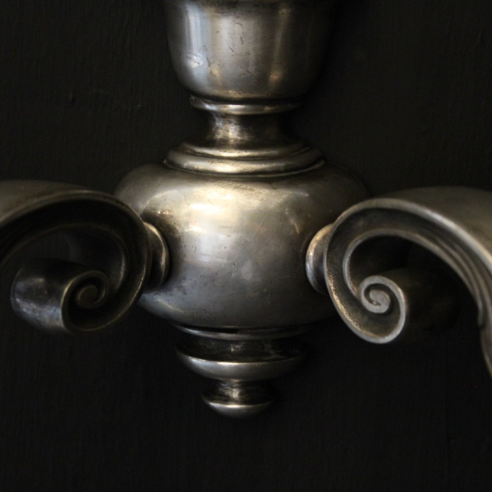 A pair of antique silver-plated twin-arm wall lights with scrolled branches, turned central urn backplates, and faux candle sleeves. View VIII