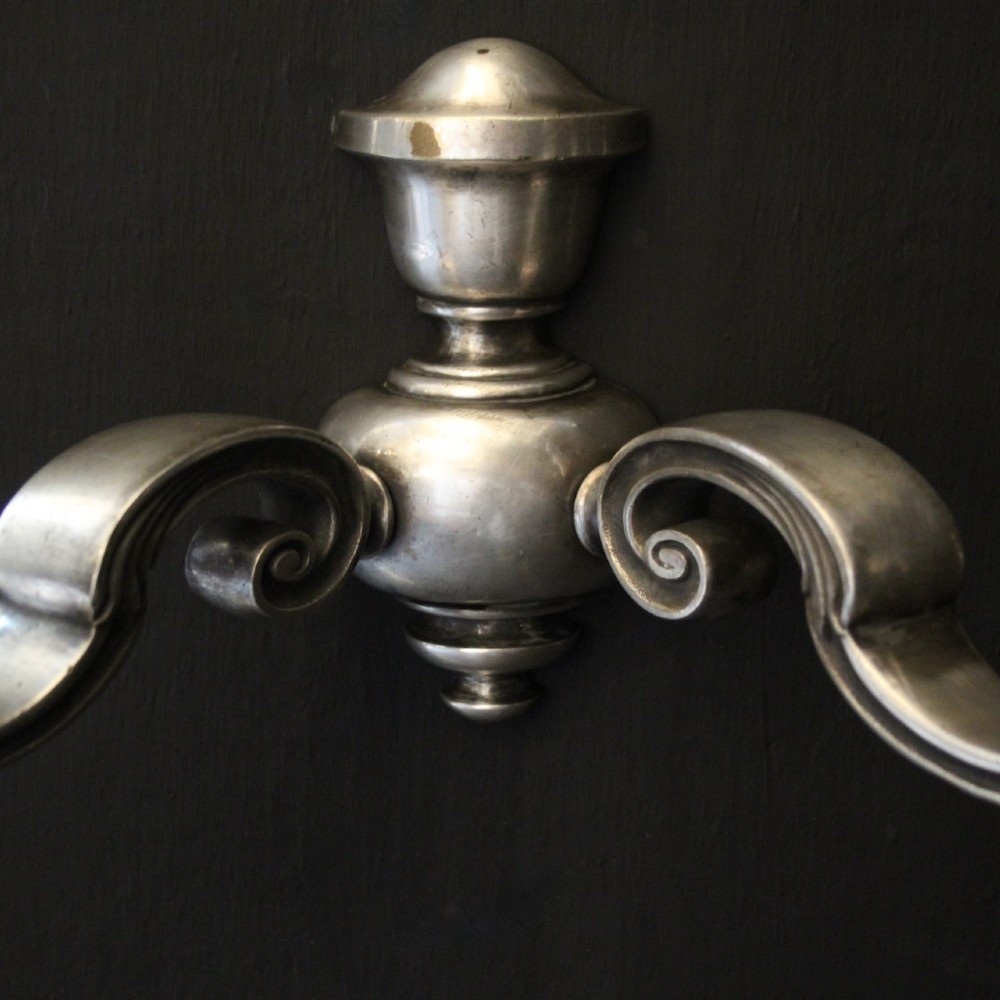 A pair of antique silver-plated twin-arm wall lights with scrolled branches, turned central urn backplates, and faux candle sleeves. View IX