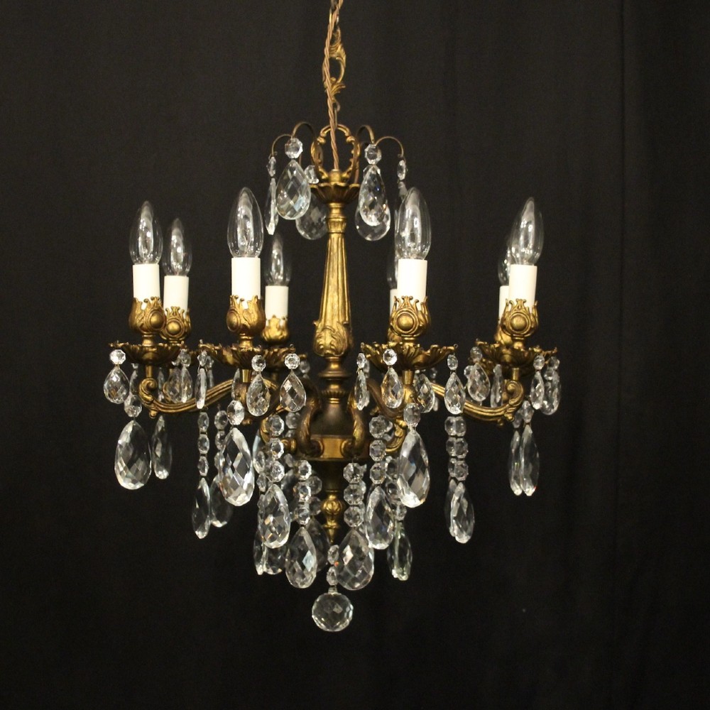 An eight-light antique French chandelier crafted from gilded metal featuring scrolling arms and clear cut glass crystal drops.