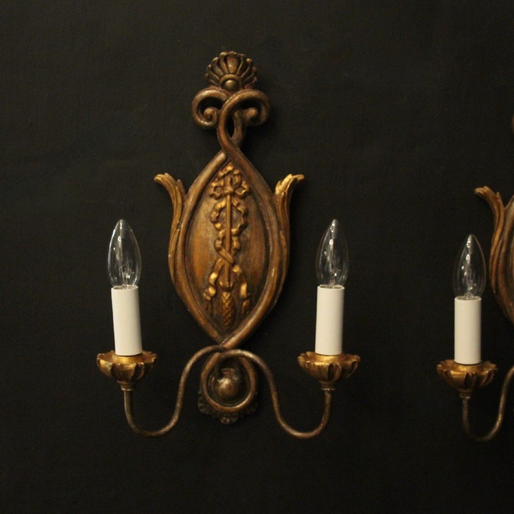 A pair of Florentine giltwood wall lights with twin curving arms, carved bow motifs, and faux candle bulb holders against a dark backdrop. View II