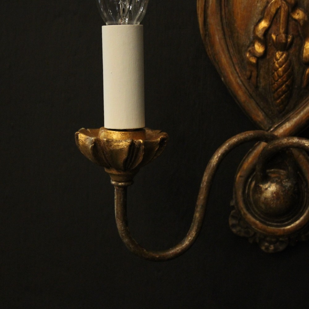 A pair of Florentine giltwood wall lights with twin curving arms, carved bow motifs, and faux candle bulb holders against a dark backdrop. View VIII
