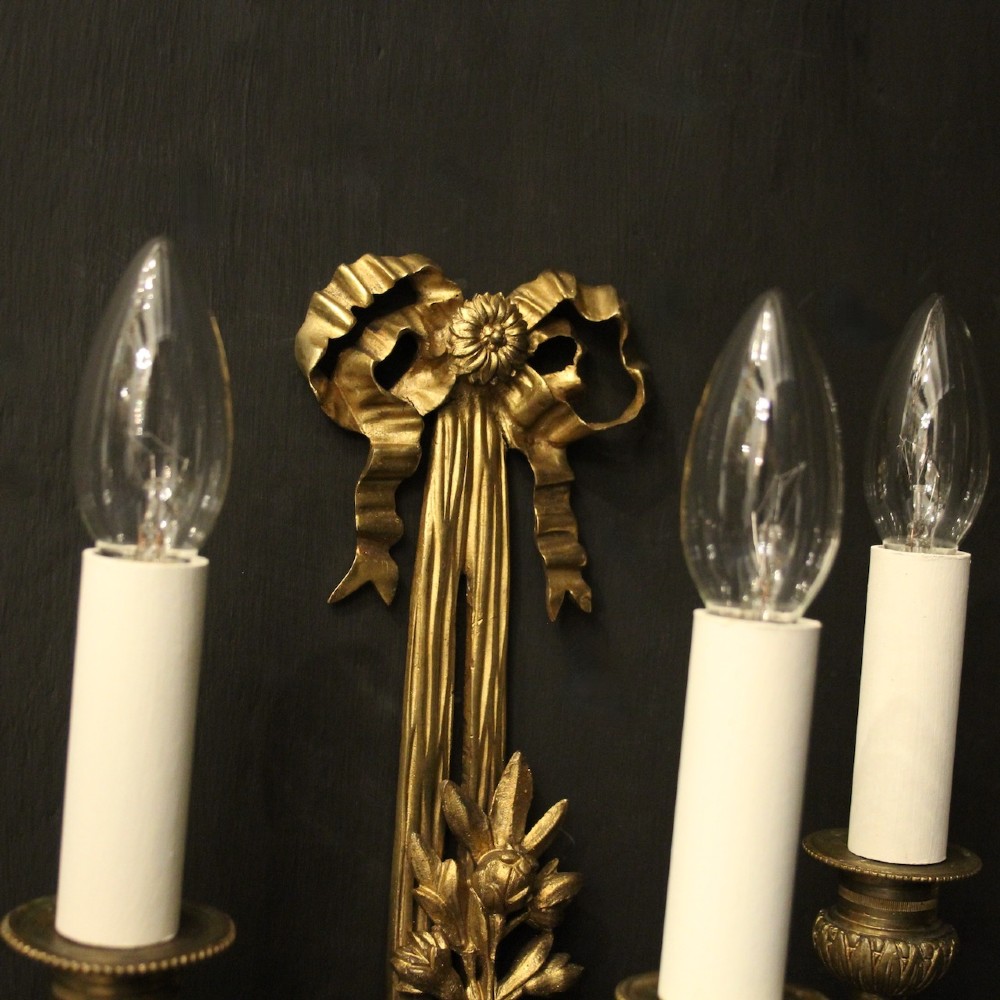 A pair of French gilt bronze three-light wall sconces featuring ribbon bow crests, tapered shafts, and scrolled candle branches. View V