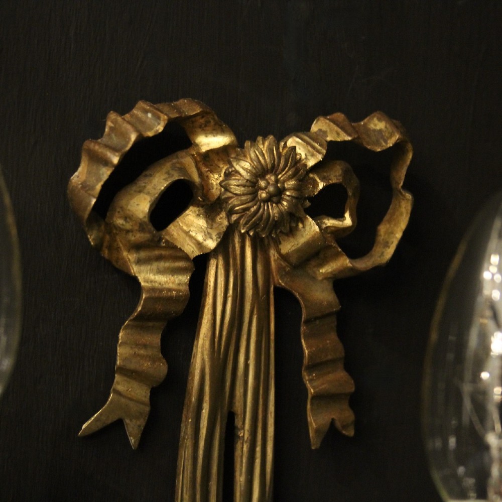 A pair of French gilt bronze three-light wall sconces featuring ribbon bow crests, tapered shafts, and scrolled candle branches. View VI