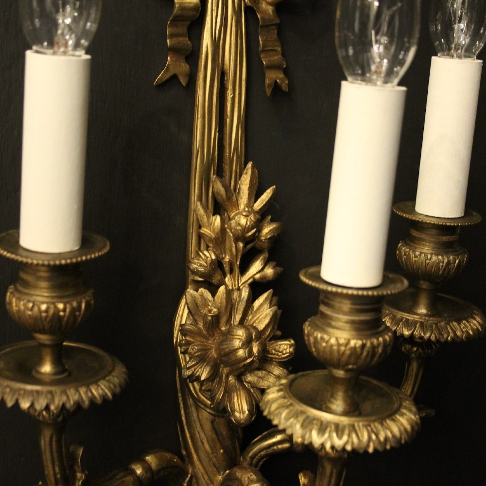 A pair of French gilt bronze three-light wall sconces featuring ribbon bow crests, tapered shafts, and scrolled candle branches. View VII