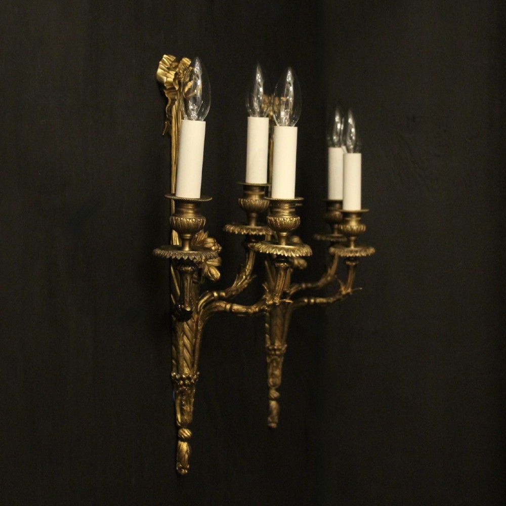 A pair of French gilt bronze three-light wall sconces featuring ribbon bow crests, tapered shafts, and scrolled candle branches. View X
