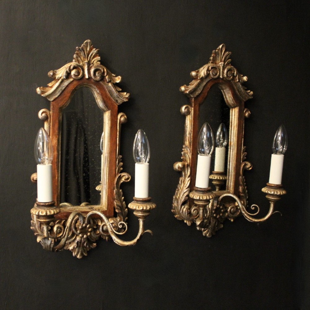A pair of carved Florentine giltwood wall girandoles featuring arched mirror backplates, acanthus cresting, and twin light arms. View II