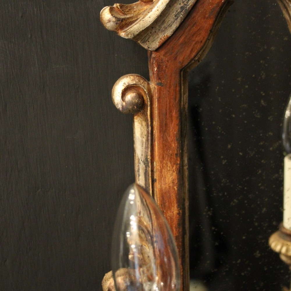 A pair of carved Florentine giltwood wall girandoles featuring arched mirror backplates, acanthus cresting, and twin light arms. View IX