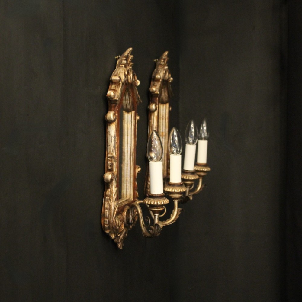 A pair of carved Florentine giltwood wall girandoles featuring arched mirror backplates, acanthus cresting, and twin light arms. View X