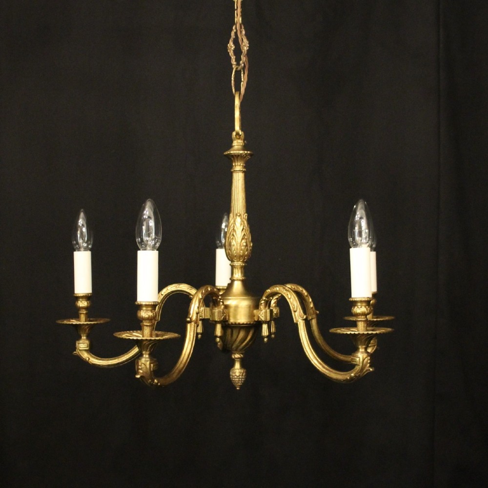 A French gilt bronze five-light chandelier featuring sweeping scroll arms, central fluted stem, decorative finial, and faux candle sleeves.