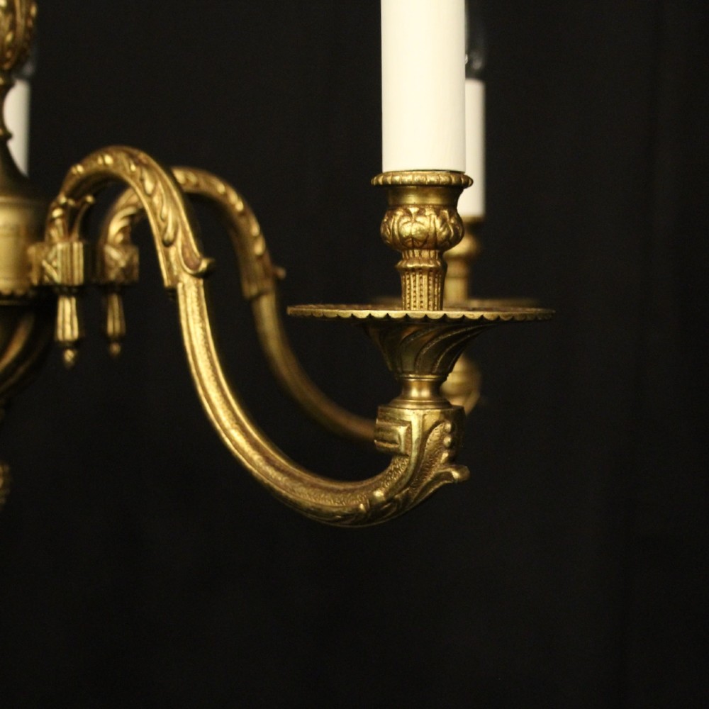 A French gilt bronze five-light chandelier featuring sweeping scroll arms, central fluted stem, decorative finial, and faux candle sleeves. View V