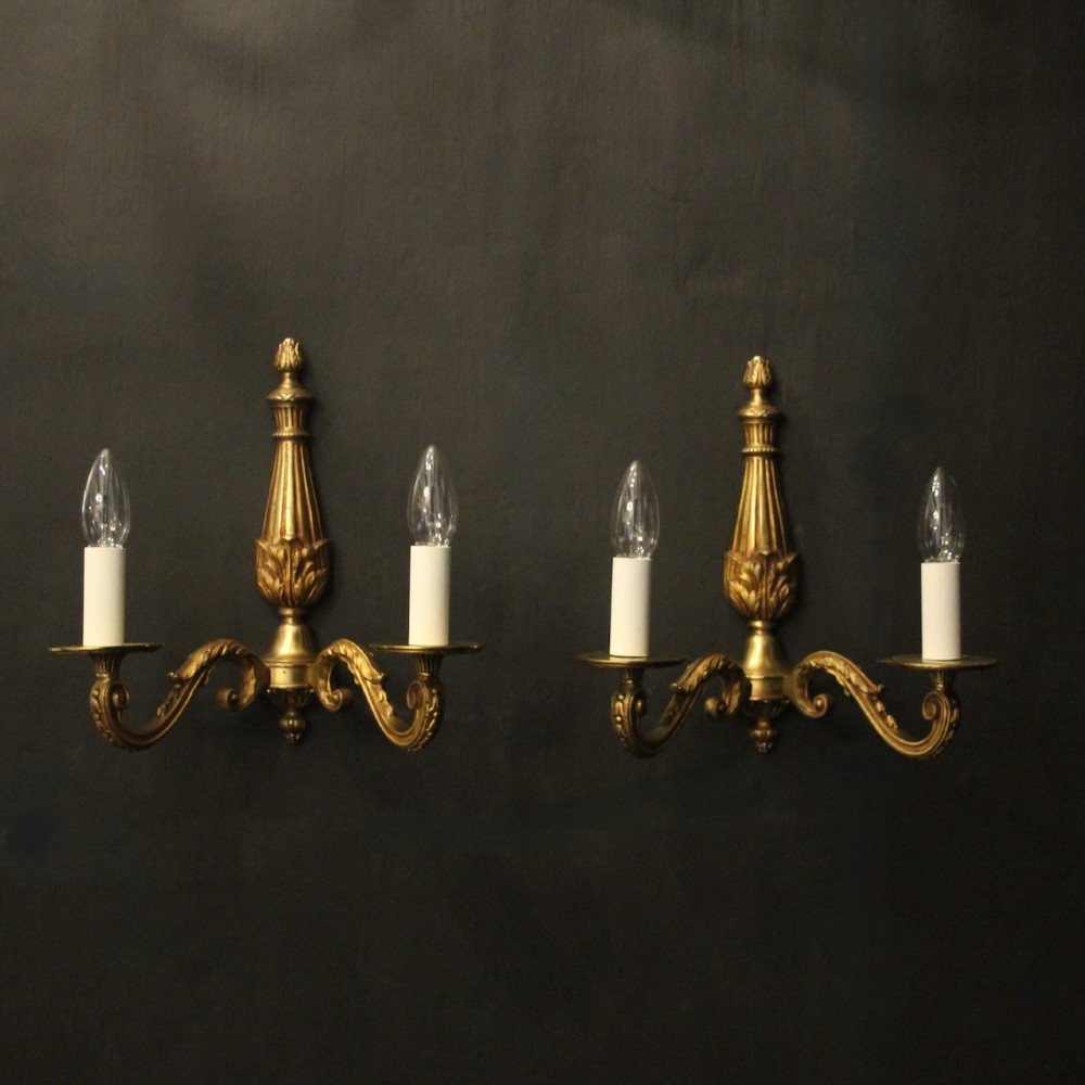 A pair of French Neoclassical gilded bronze twin-arm wall lights with acanthus leaf motifs, central fluted columns, and candle-style fittings.
