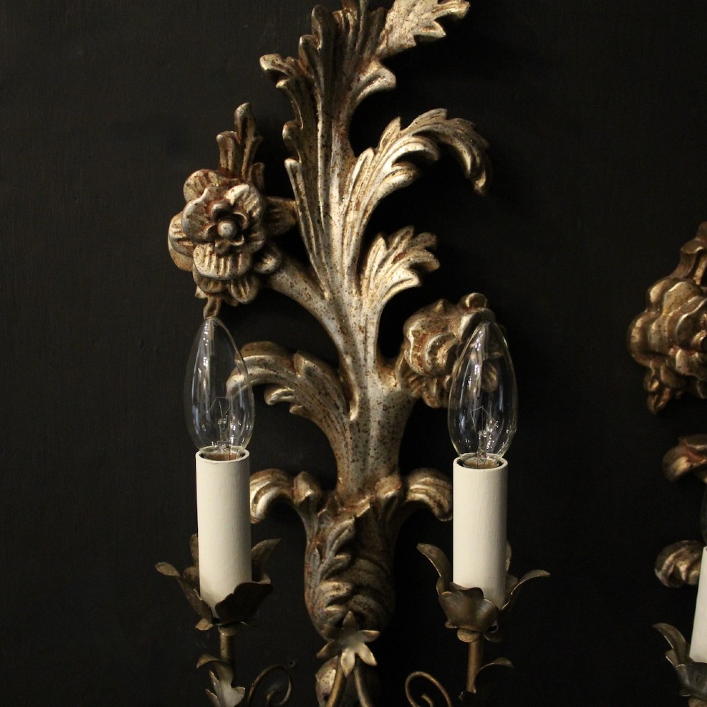 A pair of carved Florentine silver giltwood twin-arm wall sconces featuring acanthus leaf motifs and candle-style bulbs. View V