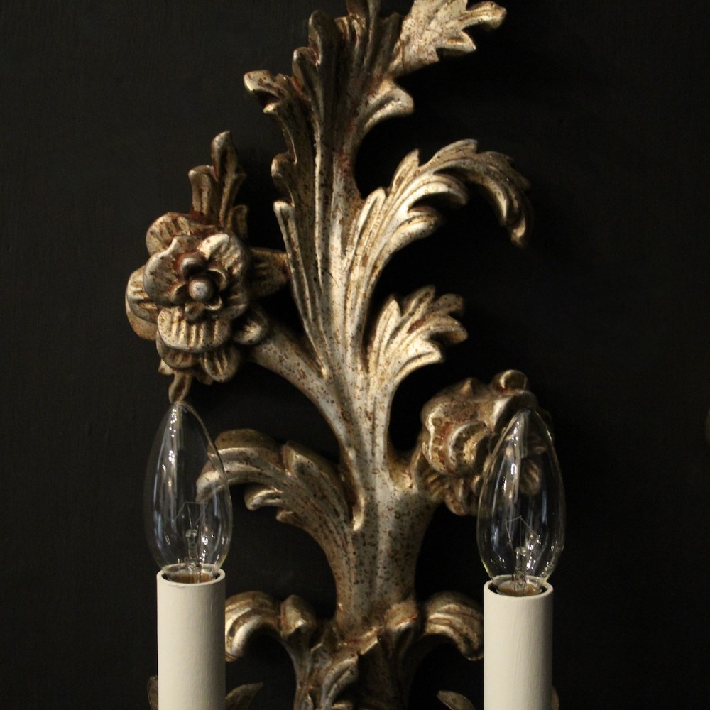 A pair of carved Florentine silver giltwood twin-arm wall sconces featuring acanthus leaf motifs and candle-style bulbs. View VI