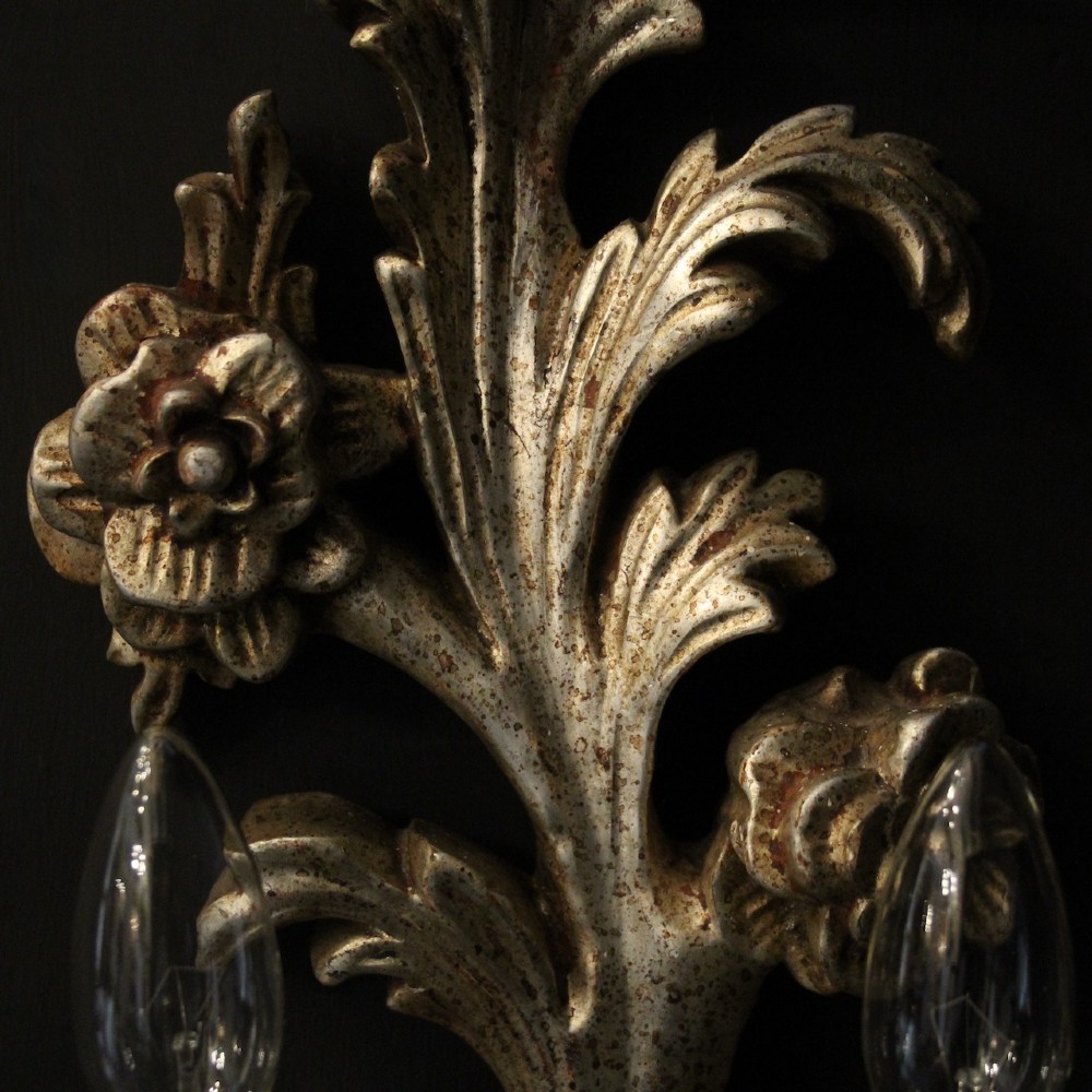 A pair of carved Florentine silver giltwood twin-arm wall sconces featuring acanthus leaf motifs and candle-style bulbs. View VII