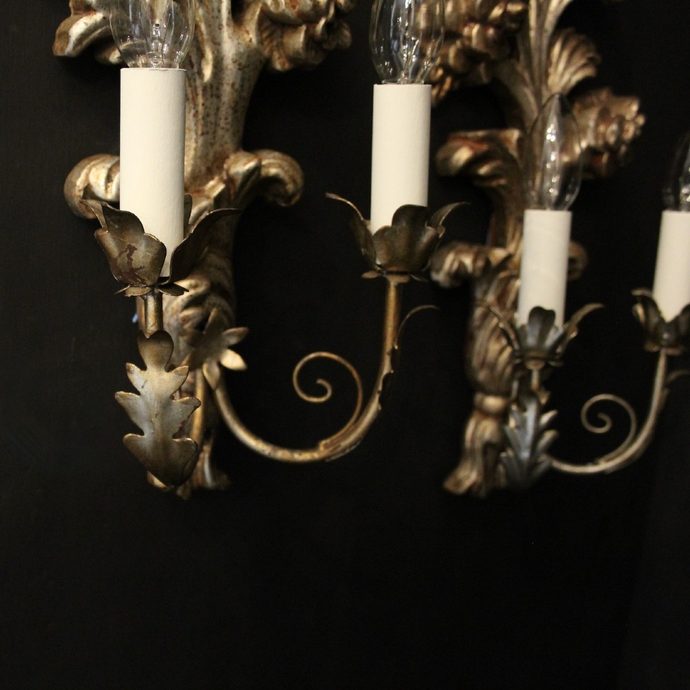 A pair of carved Florentine silver giltwood twin-arm wall sconces featuring acanthus leaf motifs and candle-style bulbs. View IX