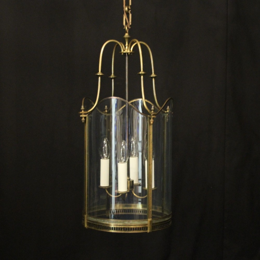 A hanging gilt brass hall lantern featuring curved convex glass panels and an internal four-candle light cluster supported by a central chain.