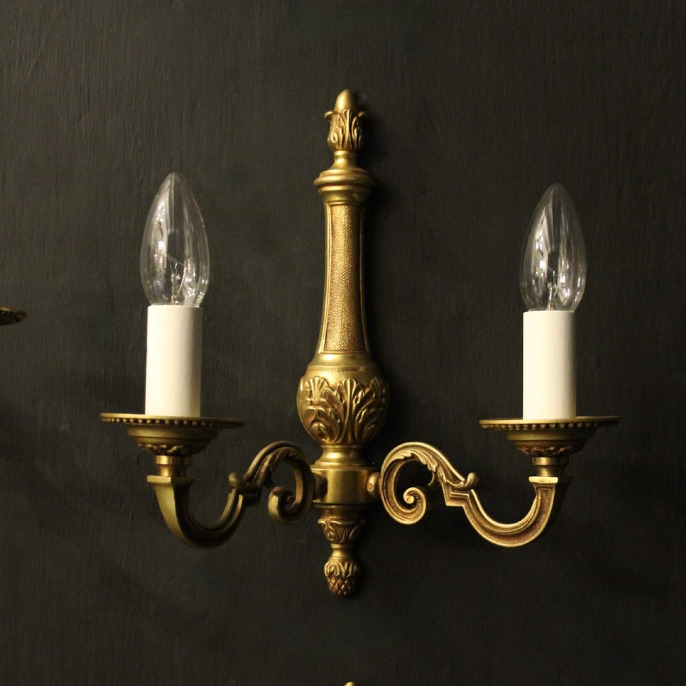 A set of four French gilded brass twin-arm wall sconces featuring scrolled arms, leaf motifs, and flame finials. View II
